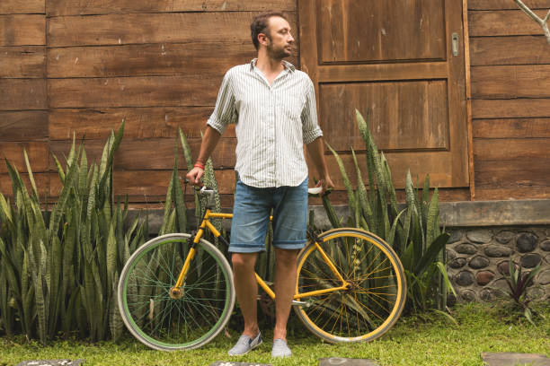 istock Modern guy standing with old bicycle in tropical garden. 918477848