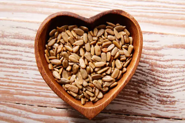 Sunflower seeds in a wooden heart shape bowl on wood board