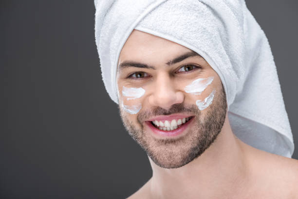 istock smiling man in towel with cream on face, isolated on grey 918484832
