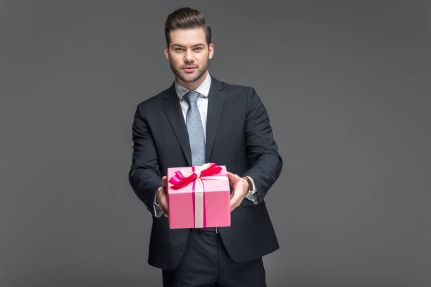 istock handsome man in suit holding present, isolated on grey 918492580