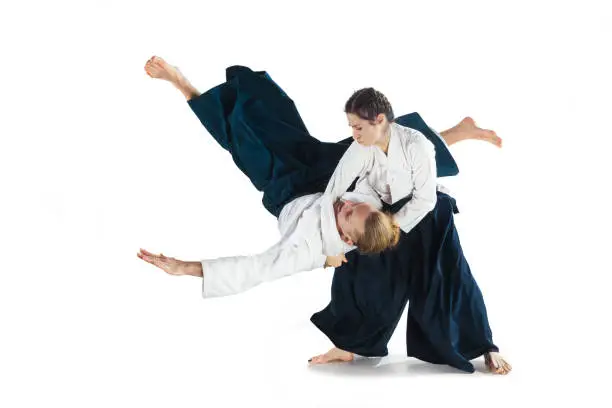 Man and woman fighting at Aikido training in martial arts school. Healthy lifestyle and sports concept. Man with beard in white kimono on white background. Karate woman with concentrated face in uniform. Isolated on white studio background