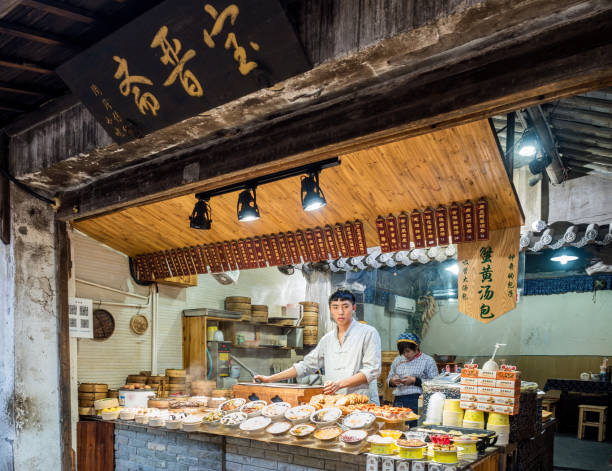 At the Zhouzhuang Water Town, Suzhou, China Suzhou, China - Nov 5, 2016: At the historic Zhouzhuang Water Town, a UNESCO World Heritage site. A food store in traditional cultural styling selling buns, noodles and other hot foods. The storekeeper in the foreground, with his assistant in the back. water town zhouzhuang china stock pictures, royalty-free photos & images