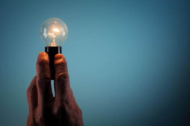 istock Male hand with incandescent light bulb on blue background. 918505402