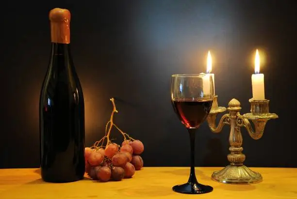 Photo of Old bottle of esteemed italian wine with glass, candle and grapes