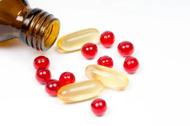 vitamin e and fish oil capsules with opened bottle on white