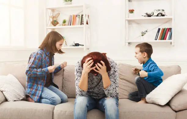 Kids having quarrel over tired mother. Mom is depressed by screaming of children. Problems of motherhood, copy space