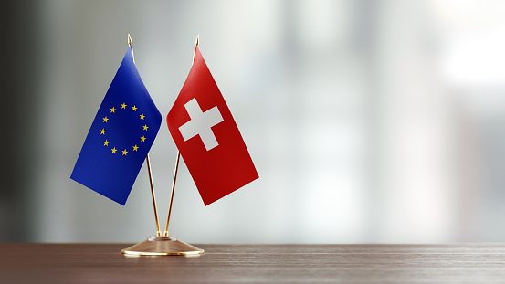 European Union and Swiss flag pair on desk over defocused background. Horizontal composition with copy space and selective focus.