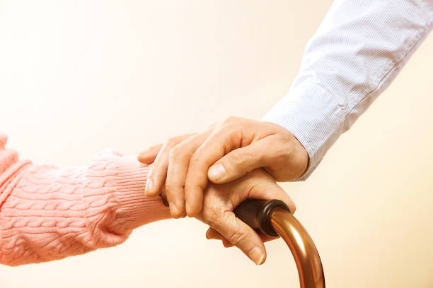 Mature female in elderly care facility gets help from hospital personnel nurse. Close up of aged wrinkled hands of senior woman. Grand mother everyday life. stock photo