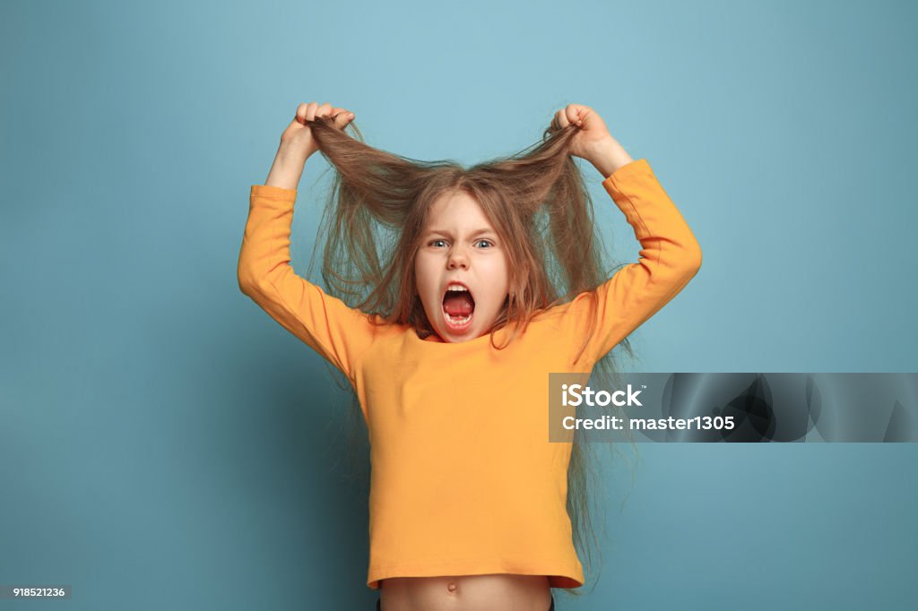 The surprise. Teen girl on a blue background. Facial expressions and people emotions concept The surprise, rage. The screaming surprised teen girl on a blue studio background. Facial expressions and people emotions concept. Trendy colors. Front view. Half-length portrait Girls Stock Photo