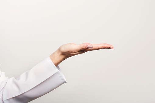 Closeup of female hand in doctors coat ponting or holding virtual object at white background. Medicine, healthcare and advertisement concept, copy space