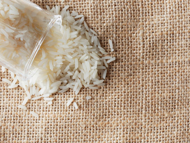 istock White raw rice drop from footed shot glass over brown sackcloth background 918522516