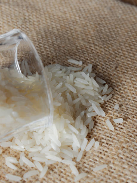 White raw rice drop from footed shot glass over brown sackcloth background