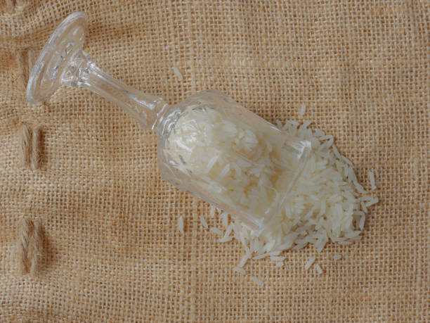 White raw rice drop from footed shot glass over brown sackcloth background