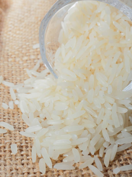 White raw rice drop from footed shot glass over brown sackcloth background