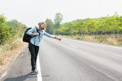 young hipster woman hitchhiking on countryside road wait for the car
