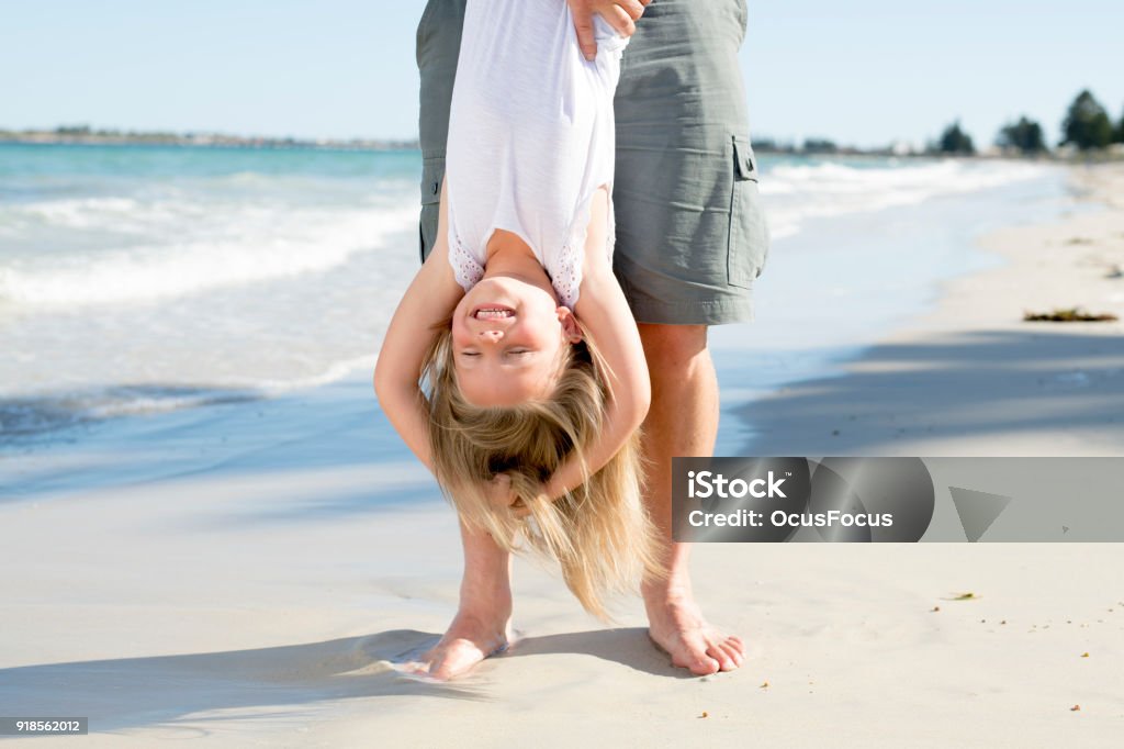 Father Holding Sweet Young And Lovely Blond Small Daughter By Her Feet  Playing Having Fun On The Beach In Dad And Little Girl Love Concept  Enjoying Summer Holidays Stock Photo - Download