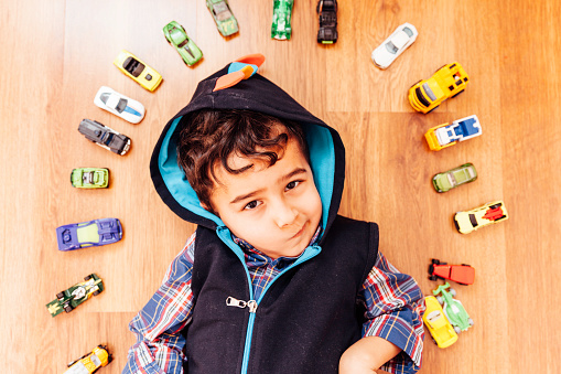 Adorable boy, lying on the parquet floor, toy cars around him