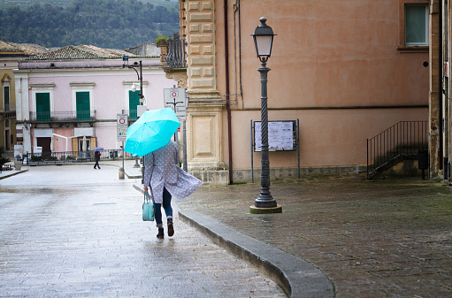 Sicily: Rainy Day in 18-Century Baroque Town; Woman  with Matching Turquoise Umbrella and Bag Walking on Cobbled Street