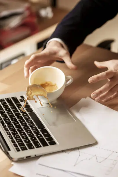 The male hands and coffee in white cup spilling in slow motion or movement on the table with laptop and documentation in the morning working day. The danger, security, safety, safeness, protection concepts. shooting for a second before an unpleasant event