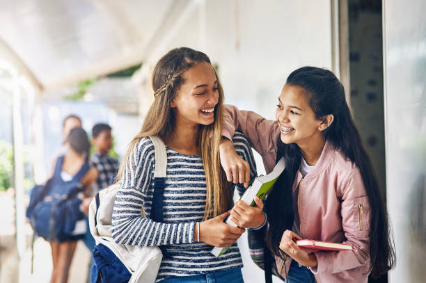 Sometimes classmates become friends Shot of two happy schoolgirls chatting in the hallway outside their classroom junior high stock pictures, royalty-free photos & images