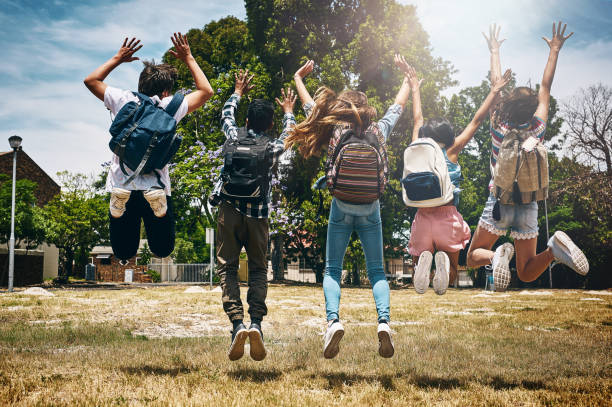 School's out! Rearview shot of a group of unidentifiable schoolchildren jumping in the park junior high stock pictures, royalty-free photos & images