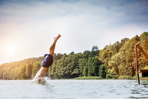 Young man diving into a lake. Careless and risky water jump. Summer vacation dangerous outdoor activity. Side view.