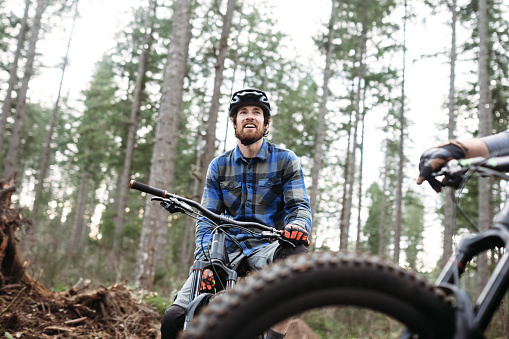 An adult man takes a break from a forest trail ride on his mountain bike, talking with a friend.  Fun and healthy lifestyle image of recreational outdoor activity.