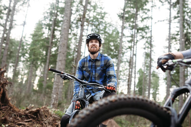 Mountain Biking Man Takes Break on Trail An adult man takes a break from a forest trail ride on his mountain bike, talking with a friend.  Fun and healthy lifestyle image of recreational outdoor activity. mountain biking stock pictures, royalty-free photos & images