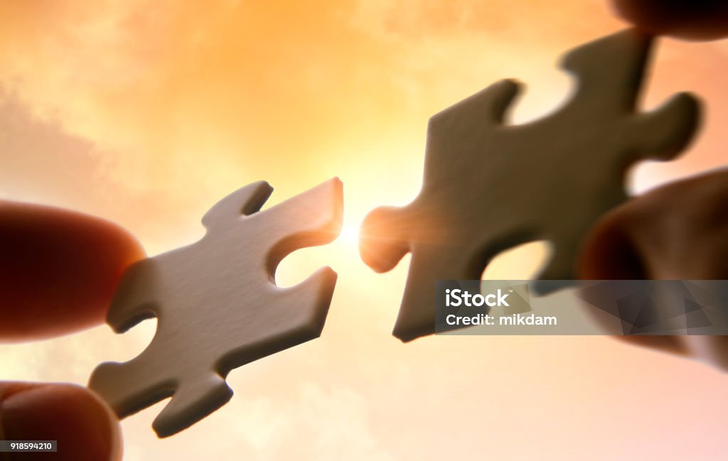 Hands putting puzzle pieces together Hands putting puzzle pieces together on sky background with sunlight Mergers and Acquisitions Stock Photo