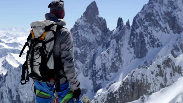 Climber mountaineer man reaching snowy mount top with ice axe in sunny day.Mountaineering ski activity. Skier people winter snow sport in alpine mountain outdoor.Back view.Slow motion 60p FullHD video