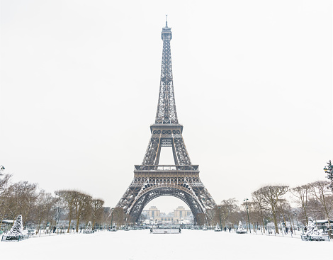 The Eiffel tower by a rare snowy day in Paris seen from the Champ de Mars, with a snow-covered lawn in the foreground and the top of the tower disappearing slightly in the mist.