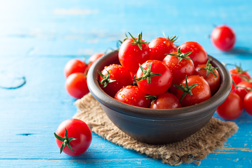 Cherry tomatoes in ceramic bowl on blue rustic wooden background. Selective focus.