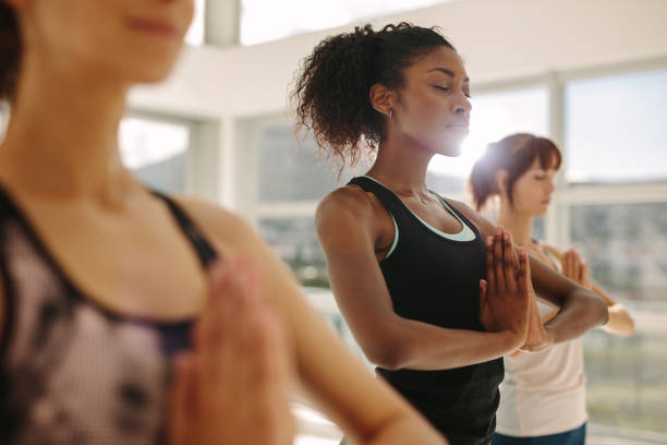 Woman practice yoga with friends in gym Fit young woman practice yoga with friends. Fitness female doing yoga meditation indoors in gym class. exercise routine stock pictures, royalty-free photos & images