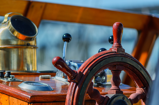 Red, old, lacquered, wooden steering wheel on a marine yacht close-up, compass in the background