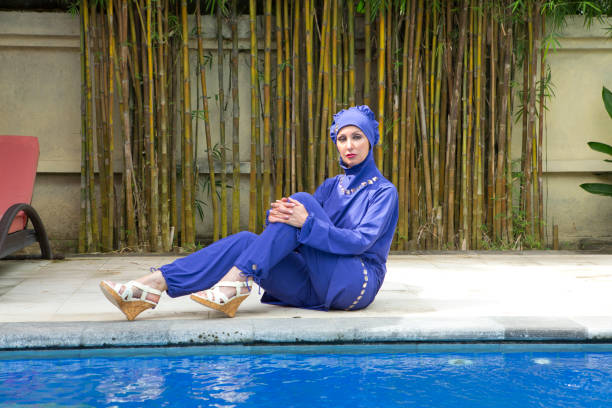 迷人的婦女在穆斯林泳裝 burkini 在游泳池邊在一個熱帶花園 - 回教泳裝 圖片 個照片及圖片檔