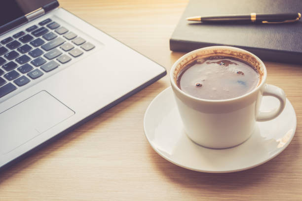 istock Close up view on work desk interior with laptop computer and morning coffee cup. Toned photo of work desk with computer and coffee cup. 918649912