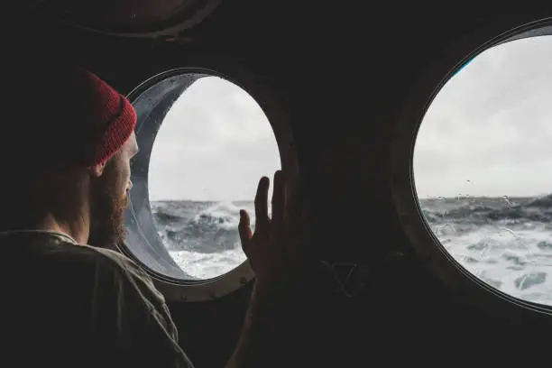 Photo of Man at the porthole window of a vessel in a rough sea