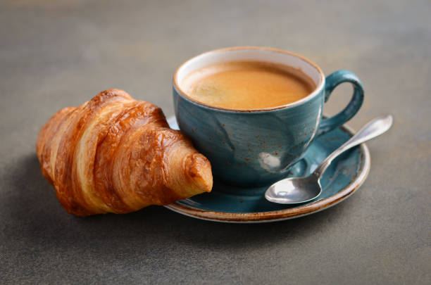 Cup of fresh coffee with croissant on concrete background.