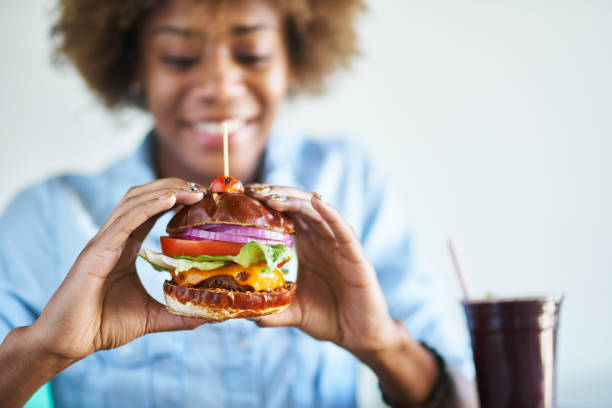 lächelnde afrikanische frau zu einen fleischlosen veganen käse burger essen - beautiful smiling vegetable calcium stock-fotos und bilder