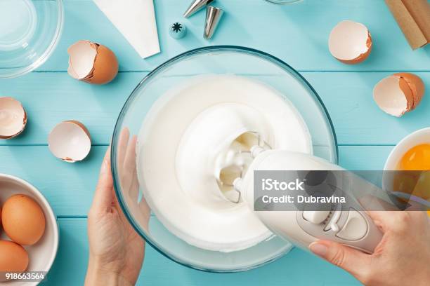 Female Hands Whipping Egg Whites Cream In Glass Bowl With Mixer On Blue Wooden Table Stock Photo - Download Image Now