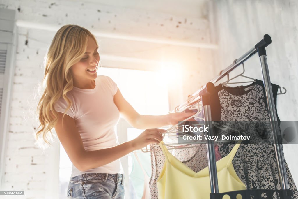 Young woman choosing clothes Attractive young woman is choosing clothes in light room. Girl in wardrobe. Clothing Stock Photo