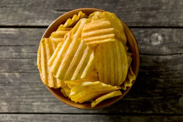 Crinkle cut potato chips on kitchen table. Tasty spicy potato chips in bowl. Top view.