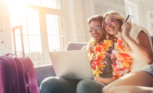 Couple preparing for travel Young romantic couple wearing Hawaii accessories and sunglasses is preparing for travel at home. Sitting on sofa with laptop and credit card in hands while suitcases are standing nearby luggage photos stock pictures, royalty-free photos & images
