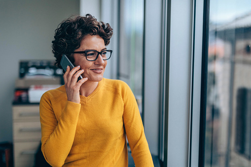 Photo of mature woman using smart phone in office near the window