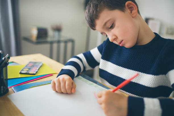 istock Young boy sitting at the table doing his school homework 918694692