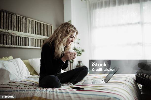 Woman Using Laptop Computer Sitting On Bed At Home Stock Photo - Download Image Now - Women, Bed - Furniture, One Woman Only
