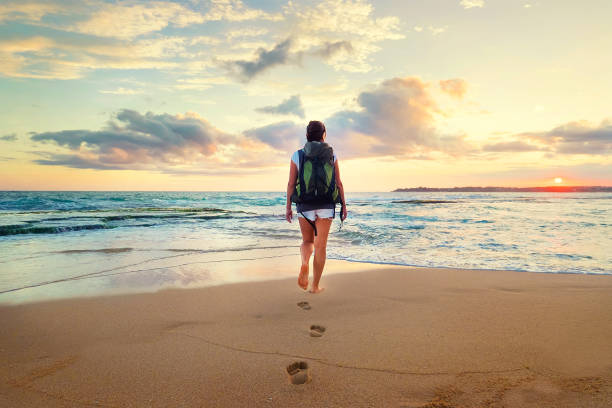 istock Woman with backpack walk on the ocean sand beach at sunset time 918699968