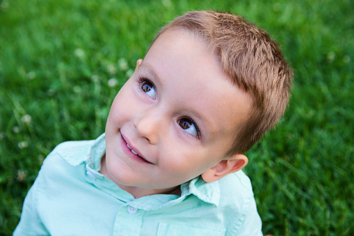 A portrait of a beautiful 3 year old boy smiling at the camera as he lies in the grass. High angle view shot with a Canon 5D Mark II. Please view many other images of children in my portfolio.