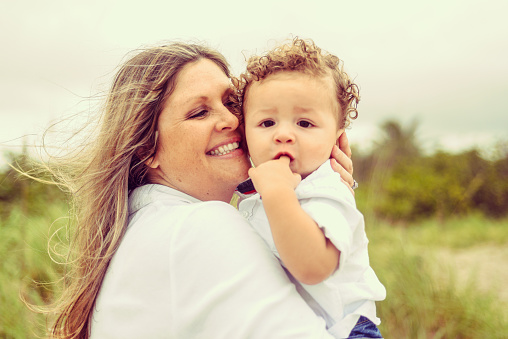 Adorable baby boy being held by his mom outdoorsin a tropical location. Mom is caucasian, boy is mixed race, candid, real, happy, people