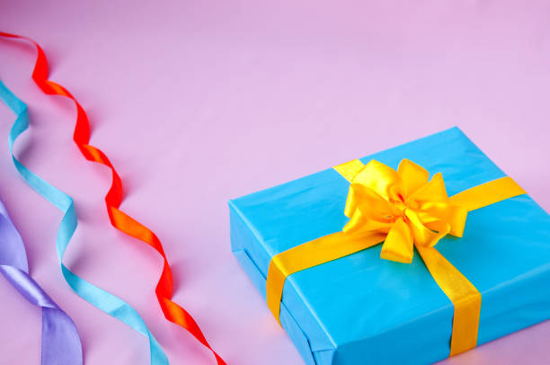istock Gift in a blue box with an yellow bow and multi-colored ribbon on a pink background 918737148